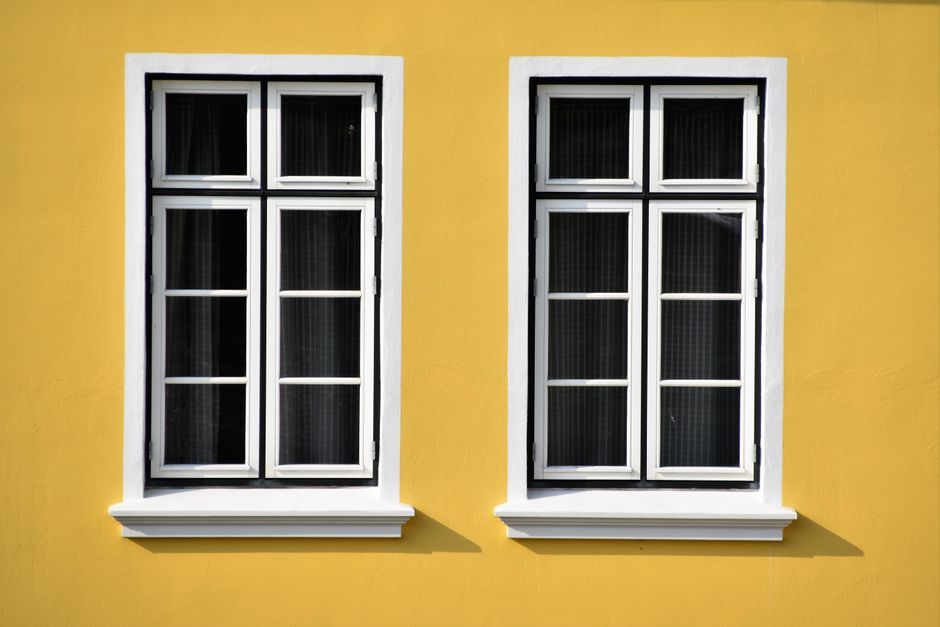 Two white framed windows set in a yellow house wall.