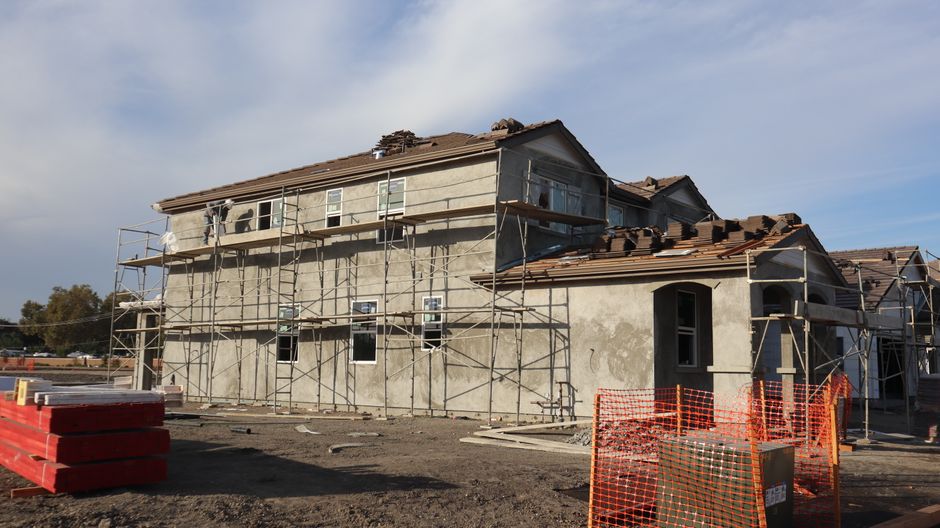 Two-story residential building under construction, featuring scaffolding and roof tiles.