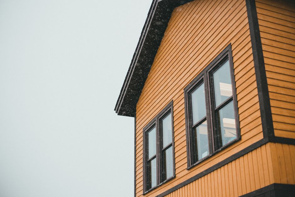 Close-up of a yellow wooden house with black trim around the windows.