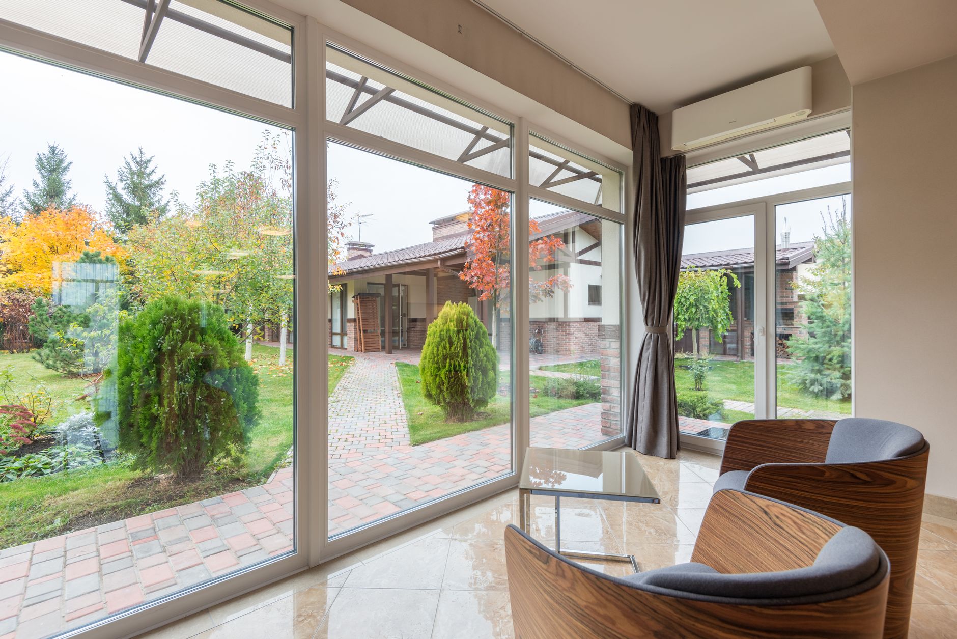 Modern house with comfortable armchairs and panoramic windows with view of green backyard with pathway and in Austin, TX